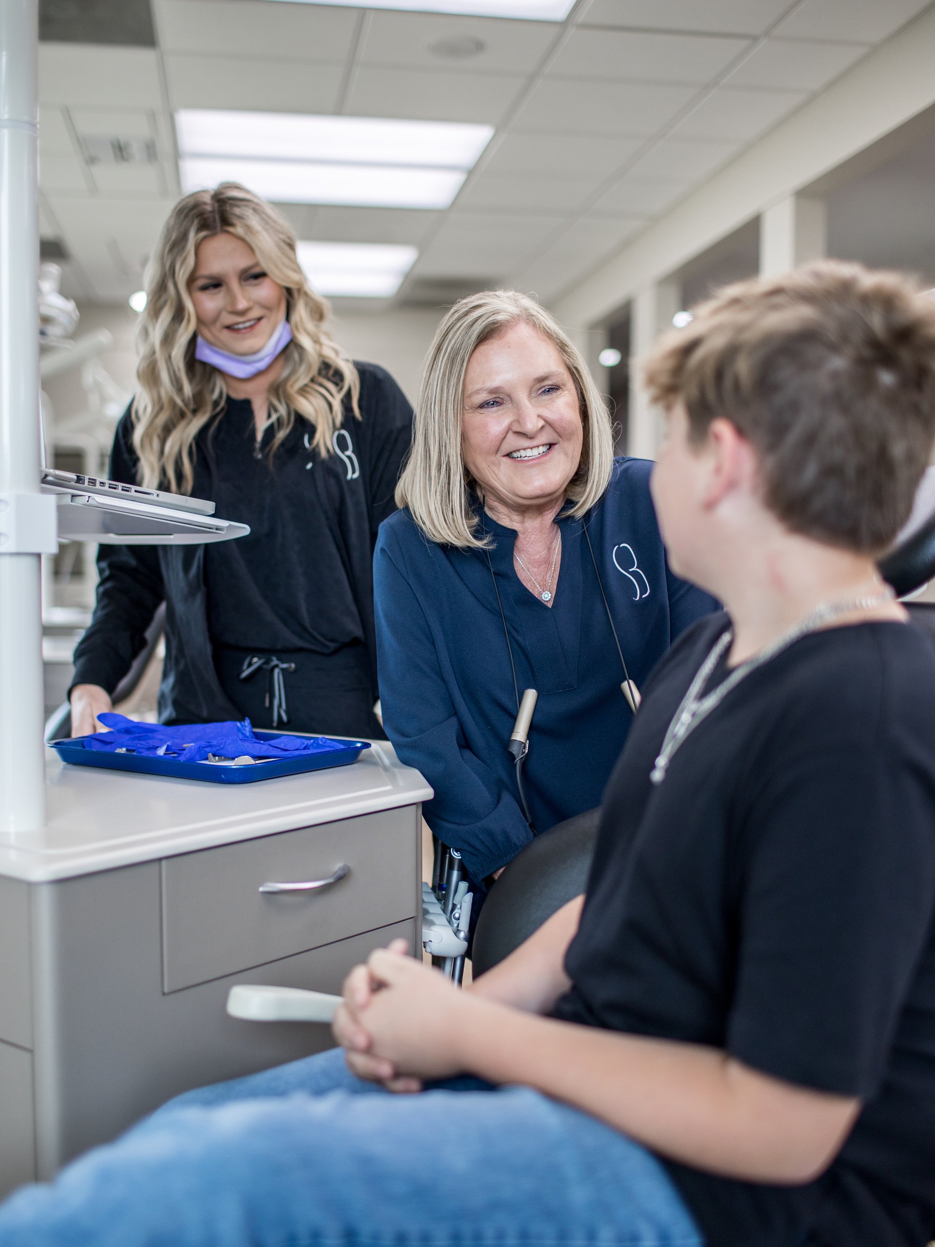 Dr. Burson smiling with a patient in the treatment room while a team member works nearby.