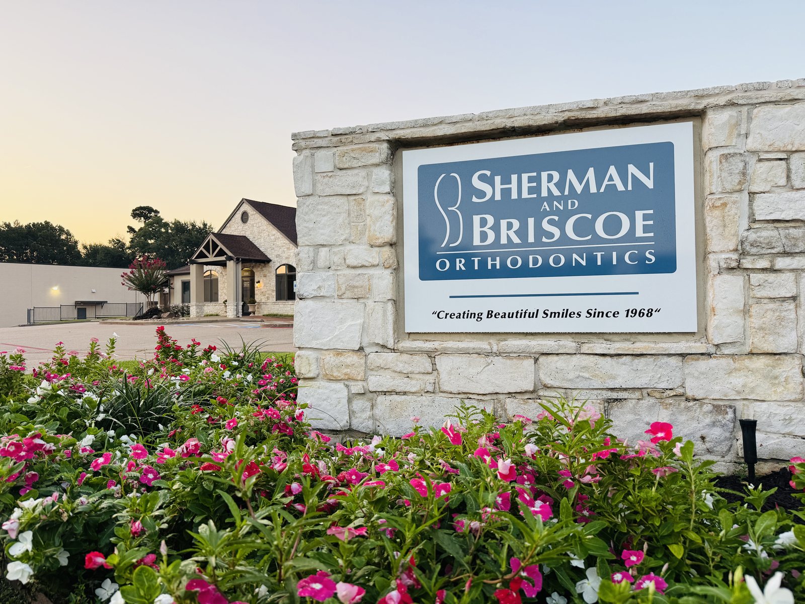 Stone Sherman & Briscoe Orthodontics monument sign at dusk with the Longview office and flowering landscape beds behind it.