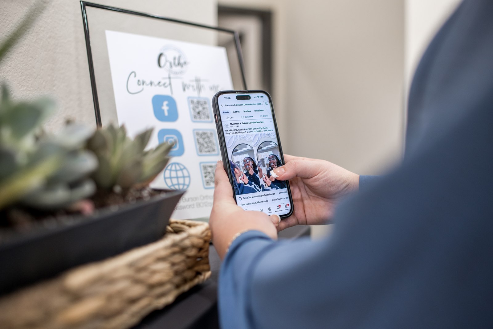 A patient viewing the practice's Facebook page on a phone beside a connect-with-us sign.