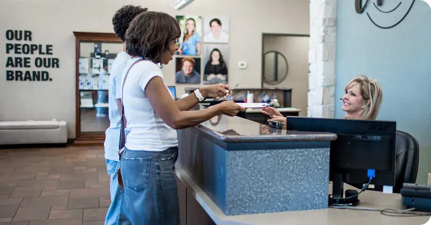 Patient checking in with a team member at the front desk beneath a people-first wall display.